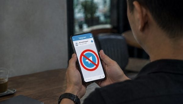 Person holding a smartphone displaying Telegram with a prohibition symbol over the Telegram logo.